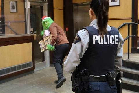 https://www.tricitylocalnews.com/wp-content/uploads/2025/12/Police-officer-watching-a-person-dressed-as-the-grinch-walk-by-with-an-arm-full-of-presents.jpg